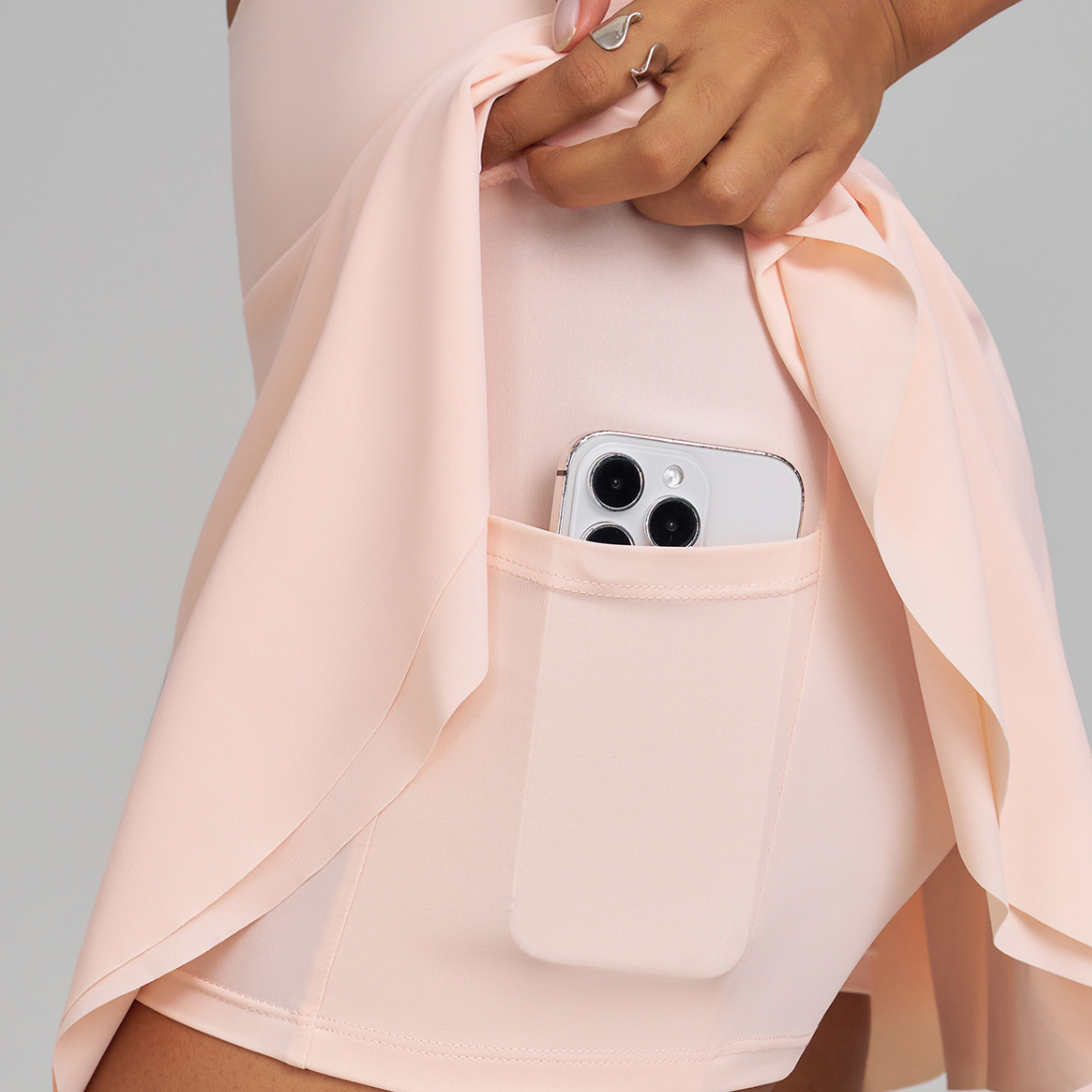 Person wearing a light pink outfit with a phone in a pocket against a gray background