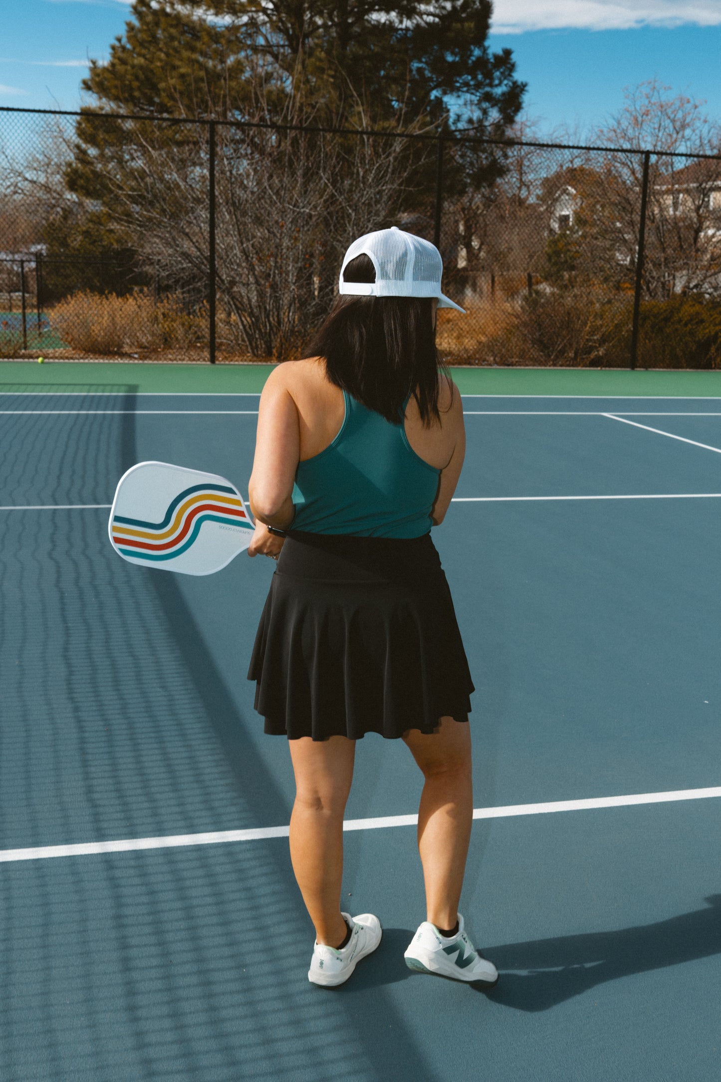Person holding a paddle on a tennis court with trees and buildings in the background